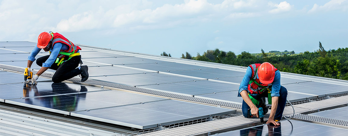 Zwei Handwerker montieren auf einem Dach Solarzellen